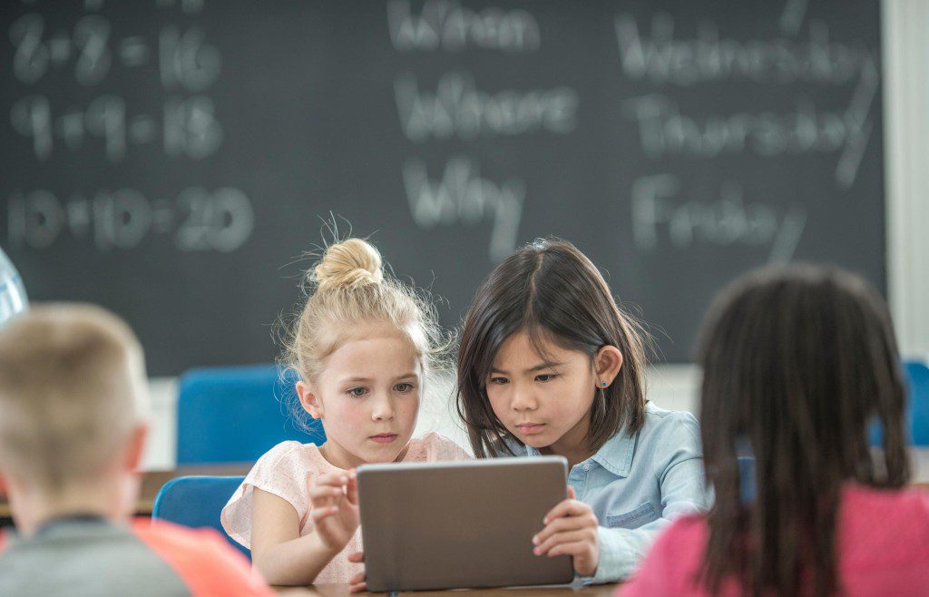 elementary age kids looking at a tablet device in a classroom