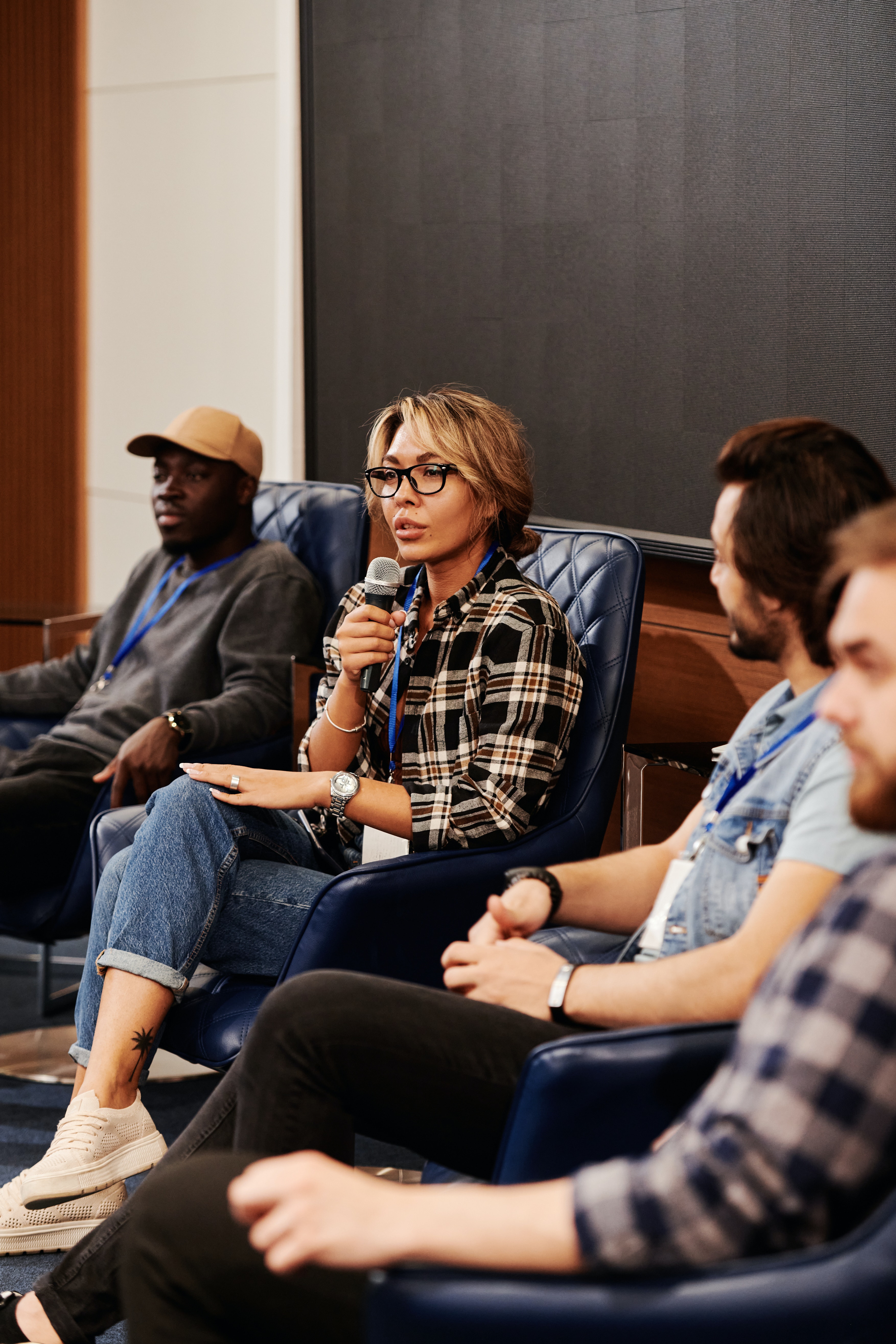 a group of conference speakers sit on a stage, with a women speaking into a microphone.