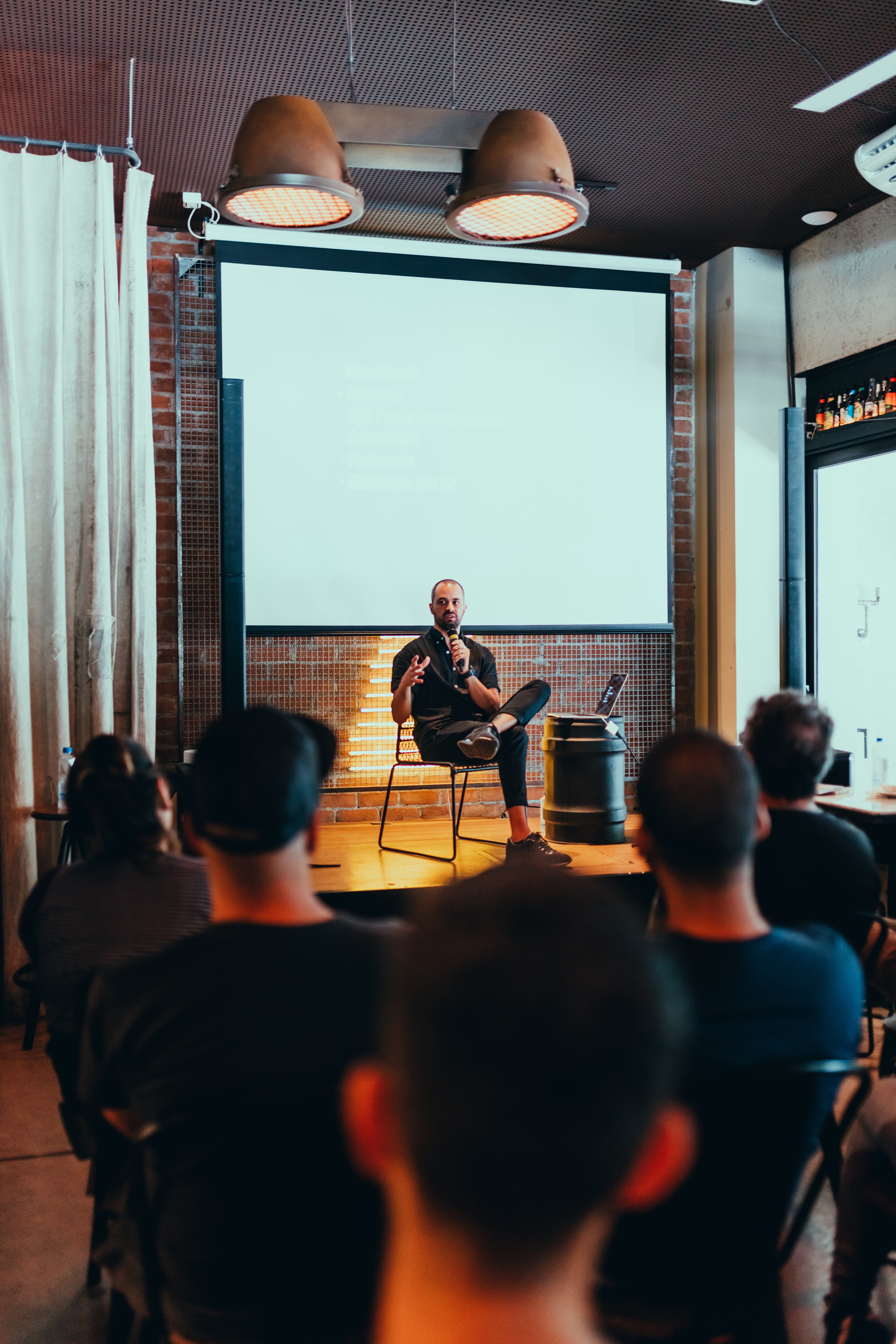 a conference speaker sits on a stage talking into a microphone in front of an audience.