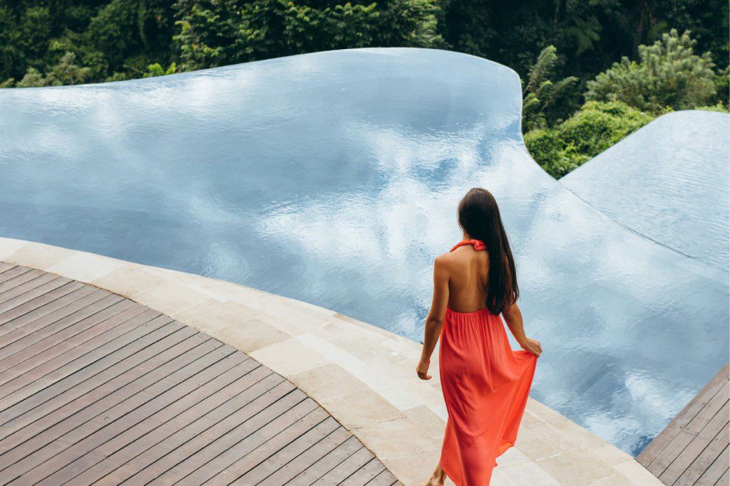 a woman wearing a red dress walking by an infinity pool